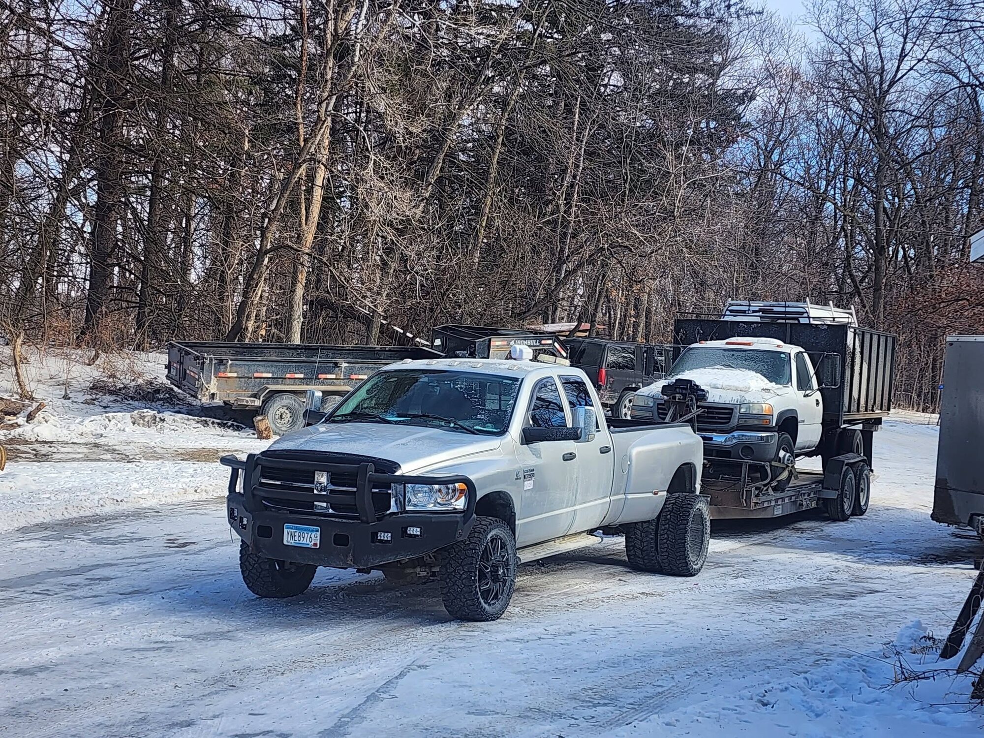 Pickup and box truck towed on a tilt trailer in winter